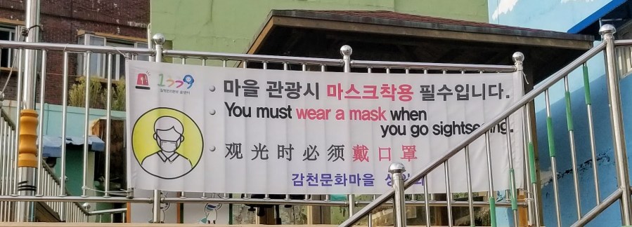 Gamcheon Cultural Village sign that says, "You must wear a mask when you go sightseeing," in English and Korean.